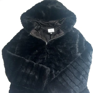 Svart fusk pälsjacka  - Mysig fuskpäls jacka med stor luva. Jackan har dragkedja framtill och är perfekt för dig som vill ha en varm och trendig look.  (Säljer då den va för stor för mig)