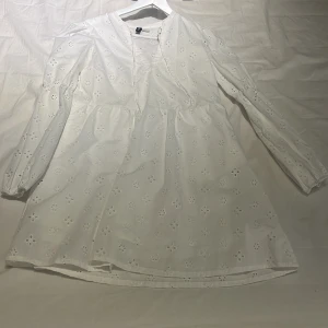 Vit broderad kortklänning från H&M - Supersöt vit klänning från H&M i storlek S med broderade blommor och hålmönster. Klänningen har långärmade ärmar, v-ringad hals och är gjord i mjuk bomull. 