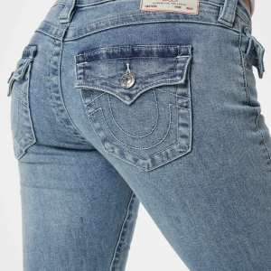 True Religion  - Snygga ljusblå jeans med bootcut passform och låg midja. Byxorna har fickor fram och bak, med dekorativa sömmar och knappar på bakfickorna. En av knapparna har lossnat men dom är fortfarande snygga och kan skicka bild på byxorna och priset kan diskuteras💕