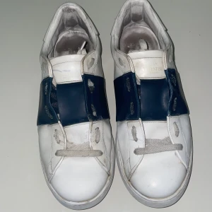 Valentino Garavani Open sneakers vit/blå - Snygga Valentino Garavani Open sneakers i vitt skinn med bred blå läderdetalj över snörningen. Klassisk rund tå och platt sula, perfekt för dig som gillar stilrena och exklusiva sneakers. Kommer med originalkartong. söker gärna byten (helst andra skor) bara att skriva vid funderingar