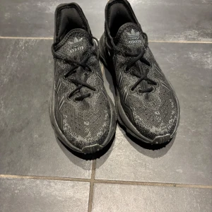 Svarta Adidas sneakers med stickad ovandel - Säljer ett par svarta Adidas sneakers med stickad ovandel och klassiska tre ränder på sidorna. Skorna har snörning och en chunky, platt sula som ger en cool vibe. Perfekt för dig som gillar sportig stil och vill ha bekväma skor med snygg design.