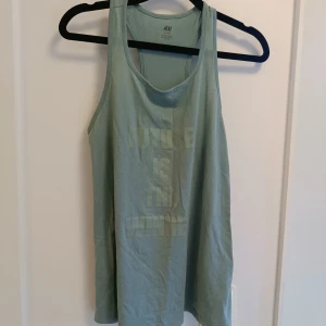 Ljusgrön linnetopp från H&M - Säljer en ljusgrön linnetopp från H&M med trycket 'FUTURE IS THE WINNER' framtill. Toppen har ärmlös design med brottarrygg och är tillverkad i mjuk bomull, perfekt för träning eller chill dagar.
