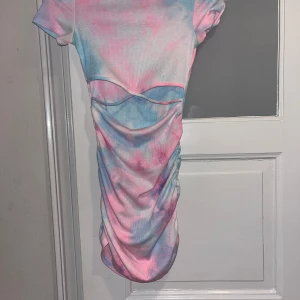 Pastell tie-dye kortklänning med rynk - Kortärmad klänning i pastellfärgat tie-dye mönster med rosa, blått och vitt. Klänningen har rynkade sidor och en markerad söm över bysten som ger en cool detalj. Mjuk, ribbad bomullskänsla och figurnära passform.