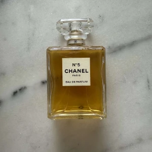 Chanel No 5 Eau de Parfum 100ml - Klassisk Chanel No 5 Eau de Parfum i 100 ml flaska. Parfymen kommer i en elegant, fyrkantig glasflaska med genomskinlig kristall-liknande kork och guldfärgad spray. Doften är ikonisk och tidlös, perfekt för dig som vill ha något lyxigt och exklusivt.
