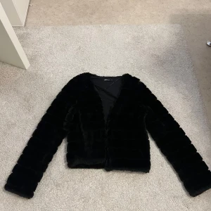 Svart pälsjacka med långa armar - Säljer en svart pälsjacka med långa armar. Jackan är fluffig och har en mjuk känsla, perfekt för dig som vill ha en stilren look med lite edge. Passar till många olika outfits och är superenkel att matcha.