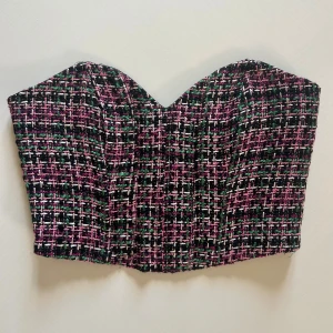 Rutig korsett-topp från Zara - Snygg korsett-topp från Zara i storlek S med rutigt mönster i svart, rosa, grön och vit. Toppen är axelbandslös med en hjärtformad överkant och har en strukturerad, lite tjockare textil som ger en cool vibe. Perfekt att styla med jeans eller kjol för en trendig look.