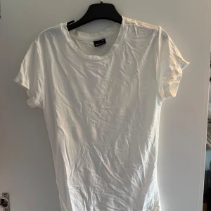 Vit t-shirt från Gina Tricot XS - En klassisk vit t-shirt från Gina Tricot i storlek XS. Modellen har rund hals och korta ärmar, perfekt för en clean och enkel look. Materialet är mjuk bomull som känns skönt mot huden. Passformen är tight och t-shirten är helt utan mönster eller detaljer.