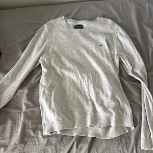 Grå bomullströja från Lexington - Snygg ljusgrå tröja från Lexington i ekologisk bomull. Klassisk rund hals och långa ärmar med ribbade muddar. Diskret Lexington-logga på bröstet ger en clean och stilren look. Perfekt för dig som gillar enkel och tidlös stil.