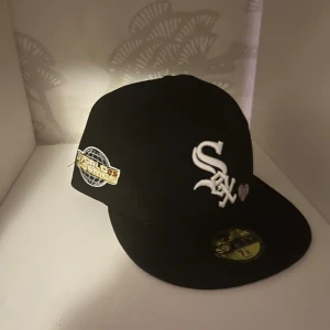 Svart White Sox keps 59FIFTY - Snygg svart keps från New Era 59FIFTY med White Sox-logga i vitt framtill och ett litet hjärta. På sidan finns en broderad World Series-patch i guld och vitt. Klassisk flat brim och strukturerad passform. Perfekt för dig som gillar sportig streetstyle. skriv för info! 