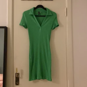 Grön ribbad kortklänning från H&M Divided - Snygg grön ribbad klänning från Divided i storlek S. Modellen är kort med krage och v-ringning, samt korta ärmar. Materialet är mjukt och stretchigt, perfekt för dig som gillar en slim passform och sportig stil. Passar dig som vill sticka ut med färg!