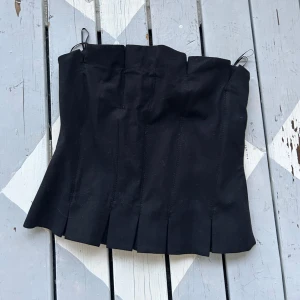 Svart korsett-topp från Zara XS - Supersnygg svart korsett-topp från Zara i storlek XS. Toppen har markerade sömmar, breda veck nertill och dragkedja i sidan för enkel påklädning. Axelbandslös design som ger en clean och edgy look. Perfekt att styla med jeans eller kjol. Defekter var där när den köptes! helt ny!!