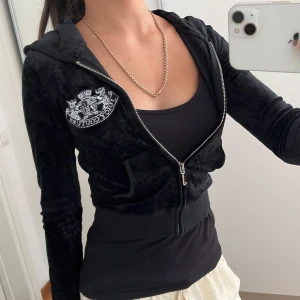Svart kofta från Juicy Couture - Säljer en svart hoodie från Juicy Couture i mjuk velour med silverfärgad dragkedja och broderad logga på bröstet och ryggen. Jackan har huva, långa ärmar och ribbade muddar. Croppad och åtsittande, sitter jätte fint. Pris kan diskuteras💕