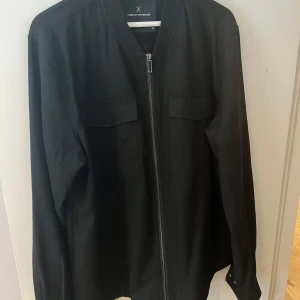 Svart overshirt från Clean Cut Copenhagen - Stilren svart overshirt från Clean Cut Copenhagen i storlek XXL men sitter som XL-L