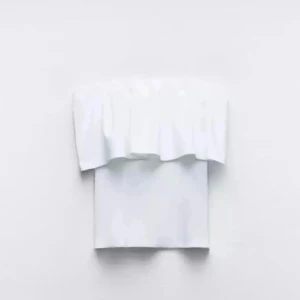 Vit bandeautopp - Säljer en snygg vit bandeau tubtopp med volangdetalj upptill. Toppen är axelbandslös och har en stilren, enkel design som ger en fräsch look. Perfekt att matcha med jeans eller kjol för en trendig outfit.