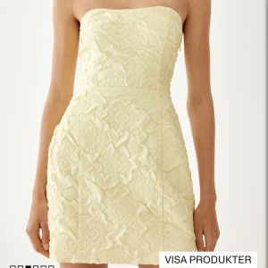 Ljusgul axelbandslös kort klänning - Superfin ljusgul axelbandslös klänning med blommigt broderat mönster. Kort modell som sitter snyggt och har en lätt A-linjeformad siluett. Perfekt för  alla tillfällen. Nypris 500kr