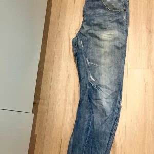 G-Star RAW 3301 ljusblå jeans - Säljer ett par G-Star RAW 3301 jeans i ljusblå tvätt med slitna detaljer och klassisk femficksdesign. Jeansen har raka ben och normal passform, tillverkade i bomull. Snyggt slitna för en avslappnad streetstil.