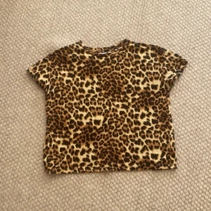 Leopardmönstrad topp från NEU XS/S - Säljer en kortärmad topp från NEU (Lager 157) i storlek XS/S med ett stort leopardmönster i bruna och beige toner. Modellen är normal passform och har rund hals. Perfekt för dig som vill sticka ut med djurprint. Materialet är mjukt och känns skönt mot huden.