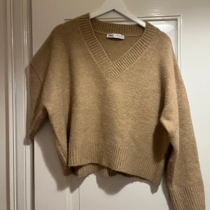 Beige stickad v-ringad tröja Zara - Mysig beige stickad tröja från Zara med v-ringning och breda ribbade muddar vid ärmslut och nederkant. Långärmad och lite loose fit, perfekt för lager-på-lager. Enkel att matcha med jeans eller kjol.