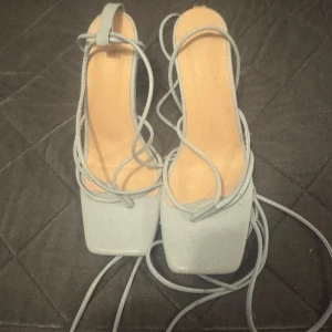 Ljusblå klackade sandaler med snörning - Snygga ljusblå sandaler med hög klack och fyrkantig tå. Skorna har långa snören som kan lindas runt benet för en trendig look. Perfekta för dig som vill sticka ut med stilrena detaljer och modern design.