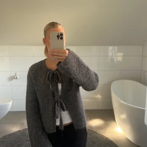 Mörkgrå kofta med knyt från Gina Tricot - Supermysig mörkgrå kofta från Gina Tricot med två knyt framtill. Koftan är fluffig och stickad med långa ärmar och rak passform.