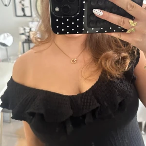 Svart offshoulder topp från Lindex - Supersnygg svart offshoulder topp från Lindex med volangdetalj längs urringningen. Toppen har en tight passform som framhäver axlarna. Perfekt för dig som vill ha en trendig och stilren look.