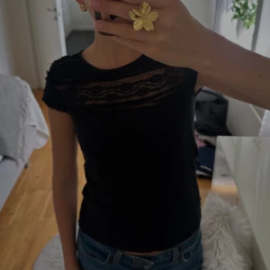 Svart topp med spetsdetaljer  - Svart topp från H&M i storlek S med snygga spetsdetaljer över axlar och bröst. Tyget är mjukt och stretchigt, perfekt för en stilren och söt look!