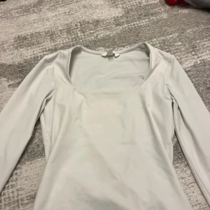 Vit långärmad topp från H&M - Säljer en stilren vit långärmad topp från H&M med fyrkantig urringning. Toppen är i mjukt stretchigt material och har en clean look som är lätt att matcha med olika outfits.