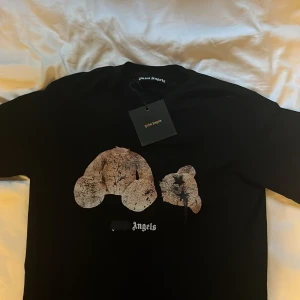 Svart Palm Angels t-shirt med ikoniskt tryck  - Svart t-shirt från Palm Angels med tryck på bröstet och logga i vitt. Oversized passform med rund hals och korta ärmar. Materialet är mjuk bomull som känns skönt mot huden. Perfekt statement-plagg för dig som vill sticka ut.