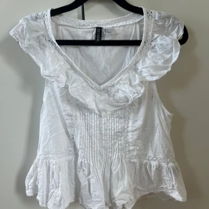 Vit volangblus från H&M Divided - Supersöt vit blus från H&M Divided med volang. Toppen är i nytt skick men säljer då den inte kom till användning! 