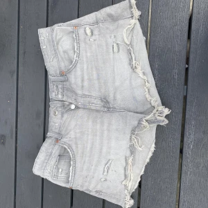 Grå jeansshorts med fransar från Zara - Snygga grå jeansshorts från Zara med slitna detaljer och fransad kant. Modellen är högmidjad och har klassiska fickor både fram och bak. Dem har en tvättad look men fina kontraster