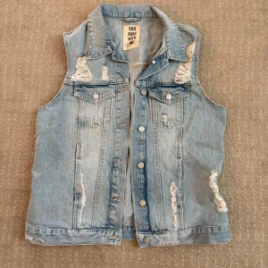 Ljusblå jeansväst med slitningar från Run Away With Me - Säljer en ljusblå jeansväst med coola slitningar och knappar framtill. 