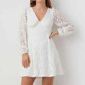 Vit blommig klänning - Supersöt vit kortklänning från Gina Tricot med blommigt mönster och långa transparenta ärmar. Klänningen har aldrig kommit till användning och har även prislapp kvar!