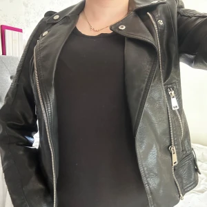 Svart skinnjacka med dragkedjor från Vero Moda - Säljer en svart skinnjacka med silvriga dragkedjor och detaljer från Vero Moda. Jackan har bred krage, snedställd dragkedja framtill och dragkedjor vid ärmsluten. Snygg passform och cool look, perfekt till många outfits. Använt endast några gånger ❤️