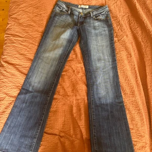 Lågmidjade bootcut jeans - Snygga blå bootcut jeans från Revers med dekorativa nitar vid fickorna framtill. Klassisk femficksmodell med dragkedja och knapp. Jeansen har en lätt tvättad look och vida ben. Perfekta för dig som gillar en retrostil.