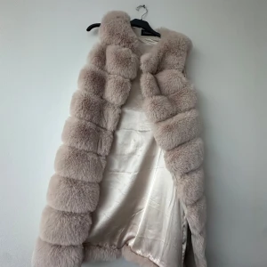 Beige pälsväst - Säljer en fluffig beige pälsväst med breda paneler och silkeslen insida. Västen är ärmlös och har en öppen front, perfekt för att lyfta din outfit med en lyxig touch.