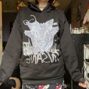 Svart hoodie med Gengar-tryck - Cool svart hoodie med stor Gengar-tryck på framsidan och texten 'INSANE'. Tröjan har huva och långa ärmar, perfekt för dig som gillar Pokémon och vill ha en avslappnad stil.