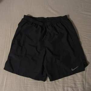 Svarta träningsshorts från Nike - Svarta träningsshorts från Nike med elastisk midja med snörning. Klassisk Nike-logga i silver på ena benet. Lätta och luftiga, perfekta för sport eller gym. Använt ett par gånger men shortsen är fortfarande i mycket bra skick. Anledning till att jag säljer är att dom är för små.