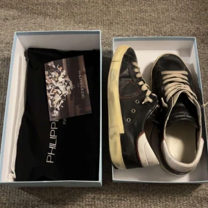 Svarta sneakers från Philippe Model - Säljer ett par svarta Philippe Model sneakers med vita snören och vit sula. Skorna har diskreta röda detaljer och är tillverkade i skinn. Klassisk låg modell med rund tå och platt sula. Levereras med originalkartong och dustbag.