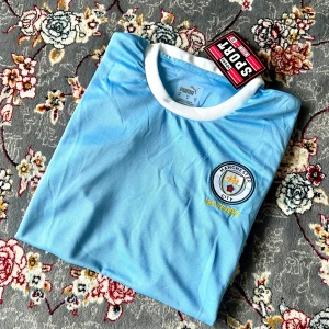 Manchester City 125 Years fotbollströja - Snygg ljusblå Manchester City fotbollströja från Puma med klubbmärke och '125 Years' broderat på bröstet. Tröjan har vit krage och vita muddar vid ärmsluten. Perfekt för dig som älskar fotboll och vill visa ditt stöd för City.