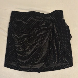 Svart sammetskjol med prickigt mönster från Zara Trafaluc - Säljer en svart sammetskjol från Zara Trafaluc med små silvriga prickar. Kjolen är kort och har en lätt draperad effekt framtill. Perfekt för dig som gillar en trendig och elegant look.