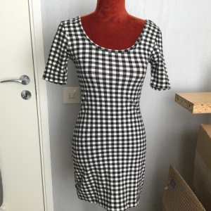 Svartvit rutig klänning från Gina Tricot S - Säljer en svartvit kortklänning från Gina Tricot med klassiskt rutigt mönster. Klänningen har rund halsringning, korta ärmar och en tight passform som framhäver figuren. Perfekt för dig som gillar en stilren och trendig look.  92% bomull 8% elastan Längd: 80 cm  Från armhåla till armhåla: 37 cm. Katter finns inhemskt!