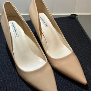 Beige pumps med spetsig tå från Yuanzhilin - Säljer ett par klassiska beige pumps från Yuanzhilin med spetsig tå och hög klack. Skorna har en elegant och stilren design, perfekta för att lyfta vilken outfit som helst. Tillverkade i syntetmaterial med glansig finish. Använt dom 2-3 gånger bara!