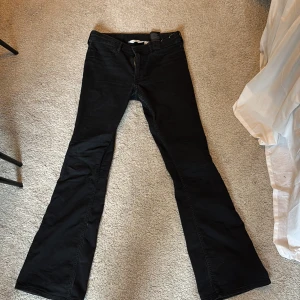 Svarta flare jeans från H&M - Säljer ett par svarta flare jeans från H&M med låg midja. Byxorna har utsvängda ben och klassisk femficksdesign. Perfekta för dig som gillar en retroinspirerad look.
