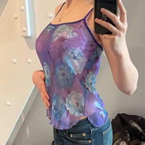 Lila blommig mesh-linnetopp - Säljer en lila mesh-linnetopp med blåa och turkosa blommor. Toppen är ärmlös med tunna axelband och har en transparent look. Tyget är stretchigt och passar både S och M 