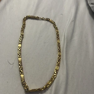 Guldfärgat halsband med mönstrade länkar - Säljer ett snyggt halsband i guldfärg med unika, mönstrade länkar. Kedjan har en cool design med både släta och texturerade partier som ger ett lyxigt intryck. Perfekt för dig som vill sticka ut lite extra.