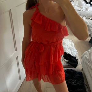 Röd volangklänning med oneshoulder - Säljer en superfin röd kortklänning med volanger och oneshoulder-design. Klänningen har knyt på axeln och flera lager volanger💕