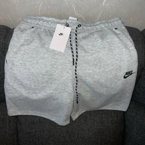 Grå mjukisshorts från Nike - Snygga ljusgrå mjukisshorts från Nike med svart logga på vänster ben. Perfekta för en avslappnad stil. 