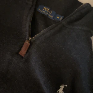 Mörkblå stickad tröja Polo Ralph Lauren - Mörkblå stickad tröja från Polo Ralph Lauren med halv dragkedja och klassisk broderad logga på bröstet. Tröjan har lång ärm och en snygg ståkrage med läderdetalj på dragkedjan. Perfekt för lager-på-lager under höst och vinter. Riktigt bra skick typ som ny // Storlek M fin och snygg pris kan sänkas vid Snabbaffär tveka ej att ställa frågor