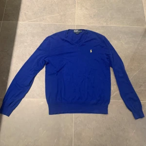Blå stickad tröja Polo Ralph Lauren - Accepterar bud! Kan gå med på en snabb affär! Nästan som ny! Snygg blå stickad tröja från Polo Ralph Lauren i slim fit-modell. Tröjan har v-ringning, lång ärm och den klassiska gula broderade loggan på bröstet. Perfekt för dig som gillar stilrena och tidlösa plagg.