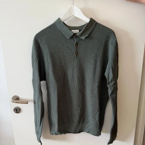 Grön pikétröja med struktur John Henric - Stilren grön pikétröja från Morris Heritage med lång ärm och snyggt strukturerat tyg. Klassisk krage och tre knappar framtill ger en clean look. Perfekt för dig som gillar en enkel men ändå uppklädd stil.